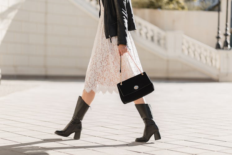 legs of attractive woman walking in street in high leather boots, fashionable outfit, holding purse,...