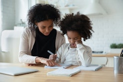 African mother helps with task little schoolgirl daughter do together schoolwork, parent explain sub...