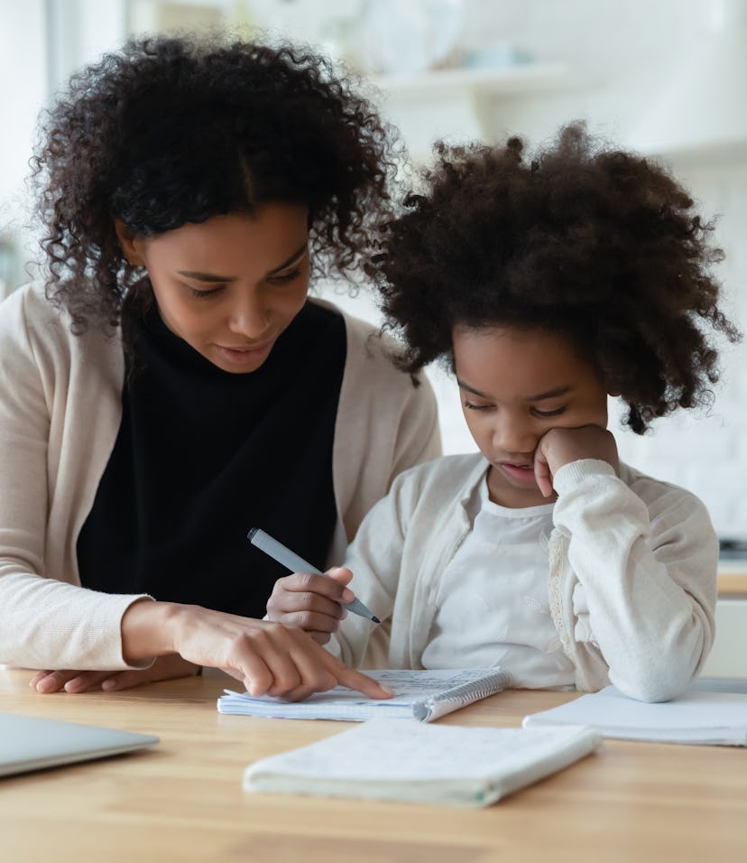 African mother helps with task little schoolgirl daughter do together schoolwork, parent explain sub...