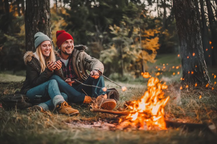 Traveler couple camping and roasting marshmallows over the fire in the forest after a hard day. Conc...