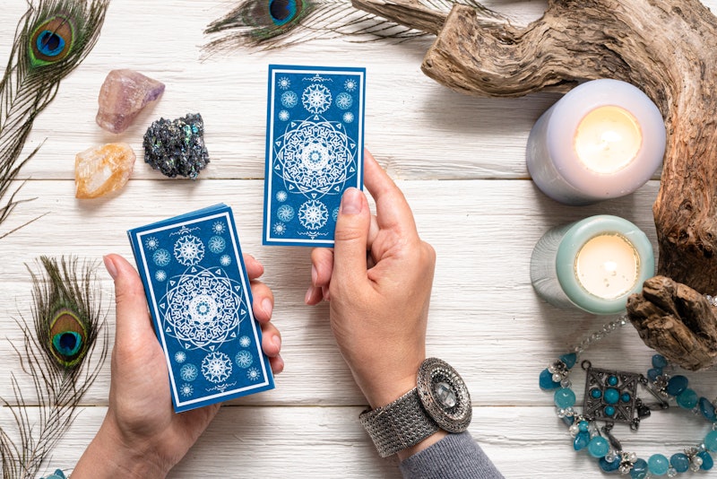 Fortune teller woman and a blue tarot cards over white wooden table background.