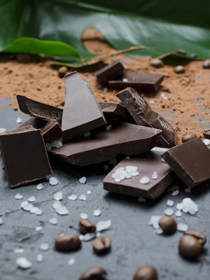 Delicious pile of pieces of chocolate, salt,cocoa powder, coffee beans on the black surface, green f...