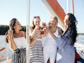 A group of friends on a cruise cheers their glasses and smile on a sunny summer afternoon.