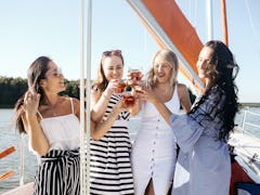 A group of friends on a cruise cheers their glasses and smile on a sunny summer afternoon.