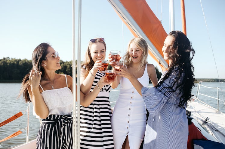 A group of friends on a cruise cheers their glasses and smile on a sunny summer afternoon.