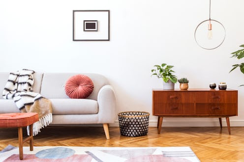 Stylish and retro interior of living room with design commode, gray sofa, round pendant lamp, vintag...