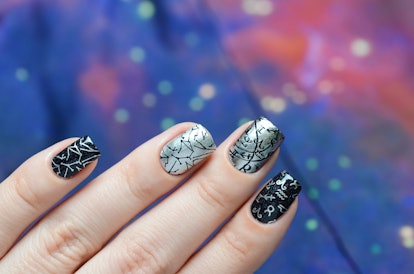 A woman's nails are painted black and silver, with various constellation and zodiac symbols on them.