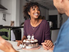 Multiethnic couple sitting at table and celebrating birthday at home. Young african girl surprised o...