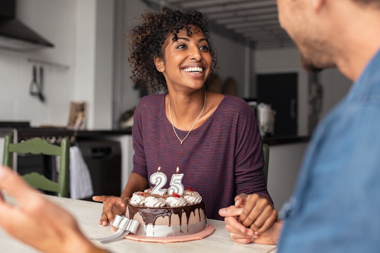 Multiethnic couple sitting at table and celebrating birthday at home. Young african girl surprised o...