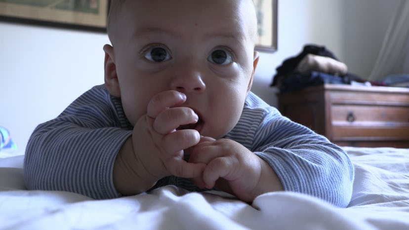 Cute baby infant toddler in bed face with hand in mouth