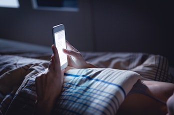 Woman using phone late at night in bed. Person looking at text messages with cell in dark home. Hips...