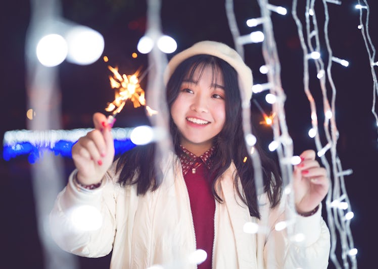 Winter night girls playing with fireworks sticks in front of LED lights .