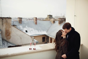 A couple kisses on a terrace next to two champagne flutes on a sunny winter day.