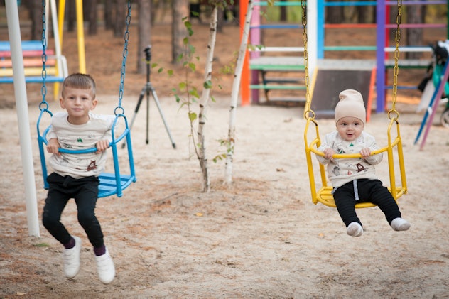 Two baby boys swinging on a swing in the park.