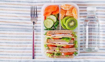 School lunch box with sandwich, vegetables, water, and fruits on table. Healthy eating habits concep...