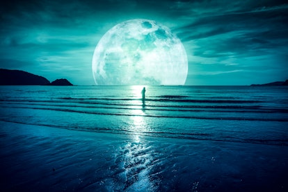 Super moon. Colorful sky with bright full moon over seascape and silhouette of woman standing in the...
