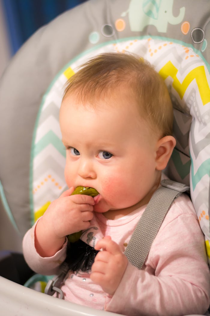 Happy baby girl eating a pickle for the first time