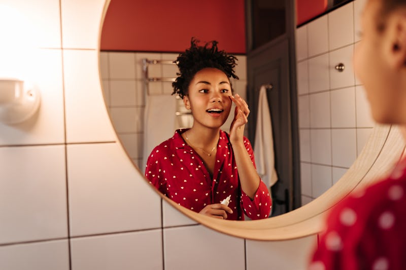 Curly woman looks in mirror and puts cream under her eyes