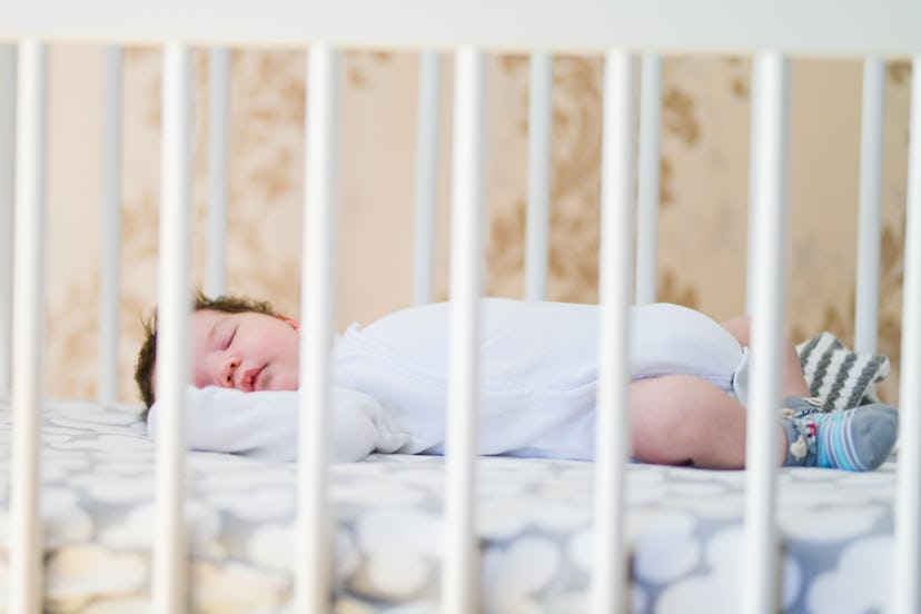 The baby sleeps in the crib. A charming baby sleeps in a crib for sleeping attached to the bed of th...