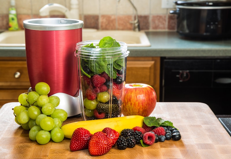 Healthy fruits with small blender on a cutting board getting ready for making a smoothie in a kitche...