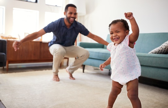 baby girl taking first steps with dad in living room