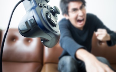 An Asian young man throwing video game controller away with anger; Concept of aggressive serious gam...