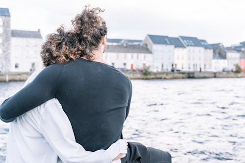 Stock photo of a Young couple hugging with their backs looking at the sea and the buildings in the b...