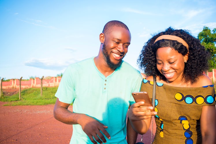 Two friends look down at a phone and laugh while walking on a pathway on a sunny summer afternoon.