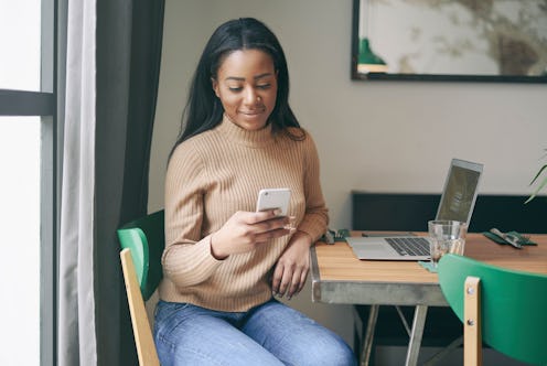 Young entrepreneur is messaging to the customers by a mobile phone and a portable computer while wai...