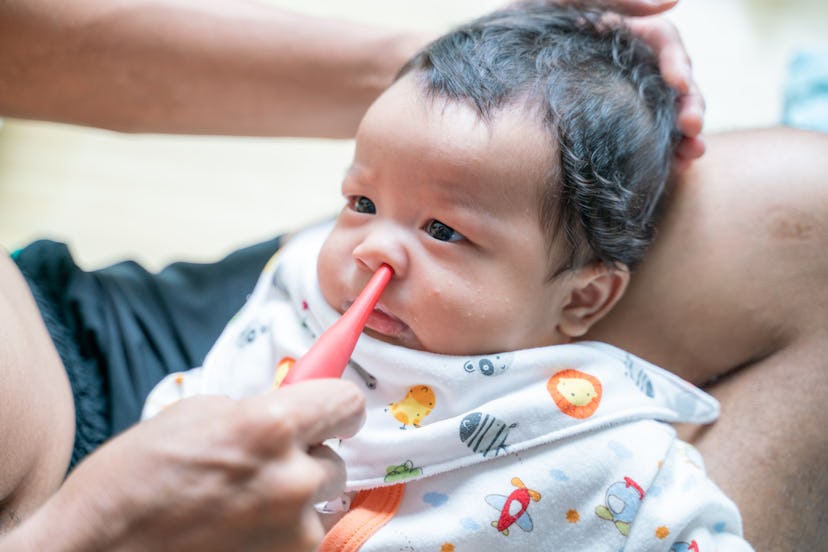 Father suctioning baby boy's nose with bulb syringe in an article about why your baby sounds congest...