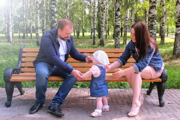 Happy family walking at weekend. Parenthood and baby care. Baby girl is trying to make first steps f...