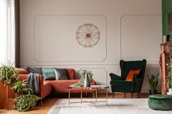 Velvet emerald green armchair with orange pillow next to corner sofa and coffee table