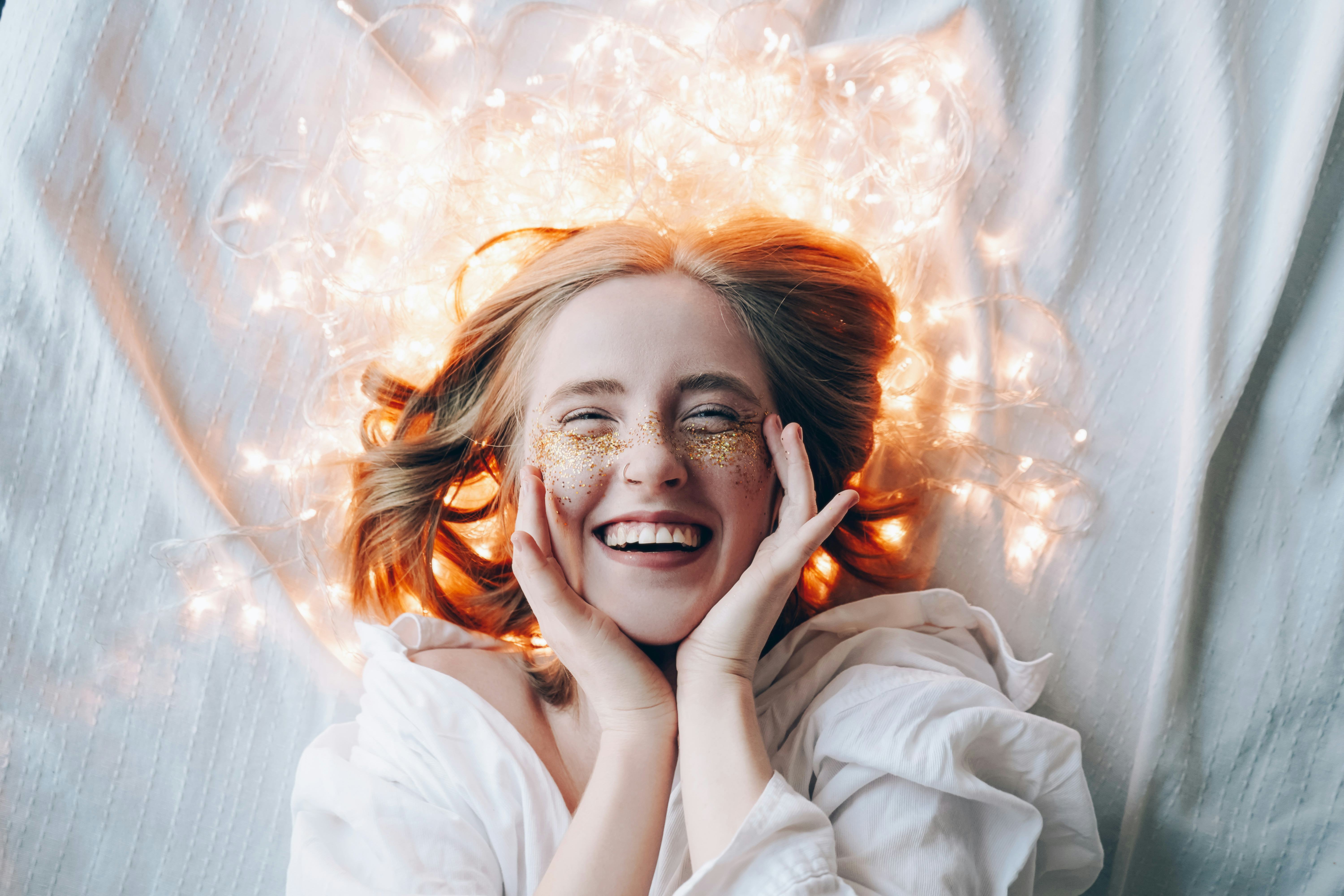 A young girl with sparkles on her cheeks lies and smiles. Christmas lights glow around. Holidays