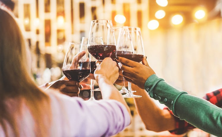 A group of friends cheers with their red wine at a bar.