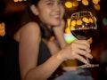 A woman smiles and holds up her wine glass filled with red wine at a restaurant.