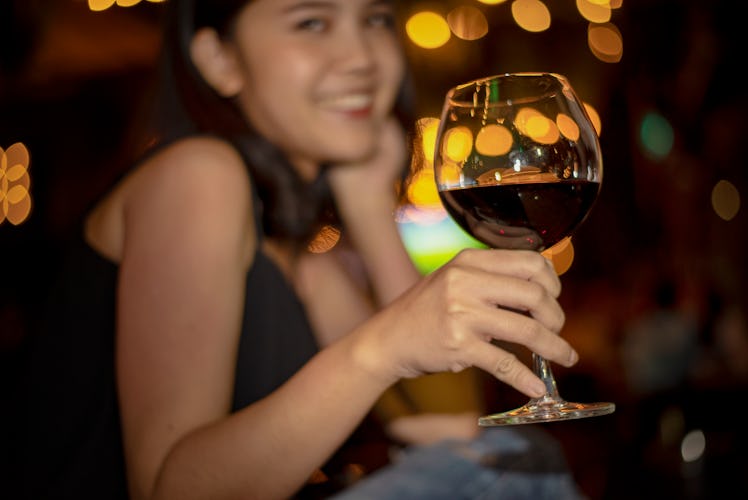 A woman smiles and holds up her wine glass filled with red wine at a restaurant.
