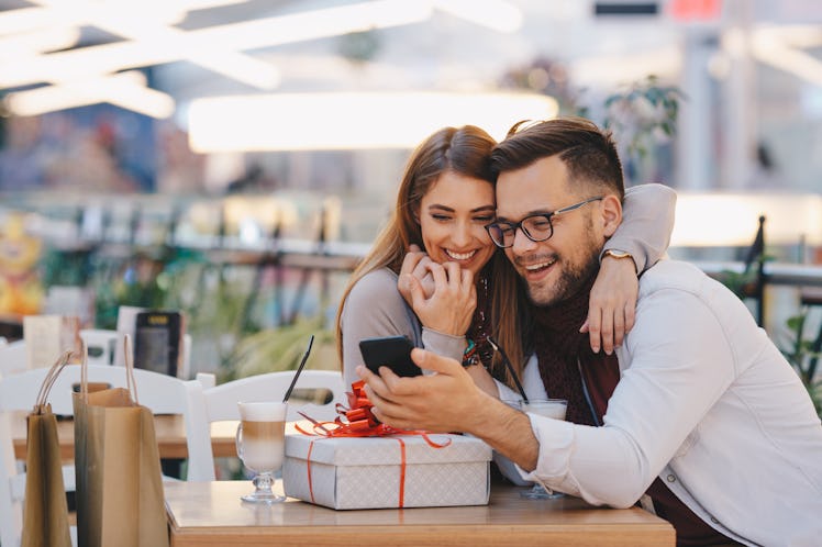 A happy couple sits at a table in a restaurant with a beautifully-wrapped gift and lattes in front o...
