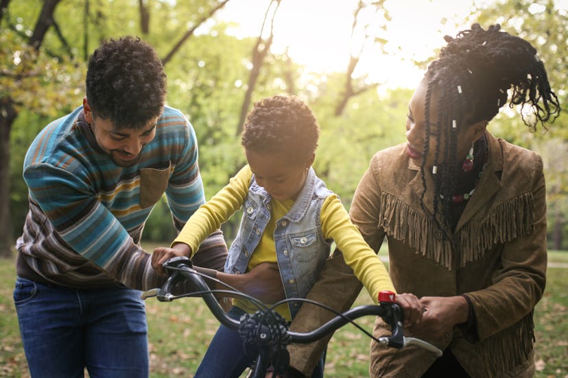 African American parents teaching their little girl to driving bike in park.