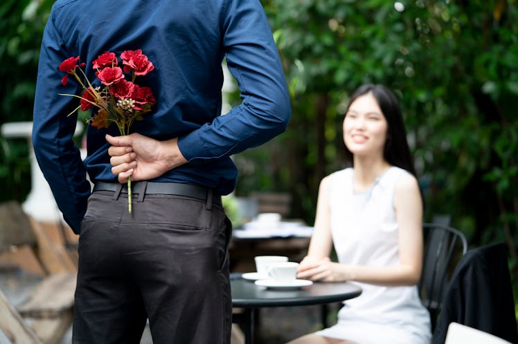 A man is proposing marriage to a smiling woman with a lovely flower bouquet in a beautiful garden, l...