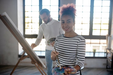 Beautiful young artist. Beautiful young artist standing in spacious room and painting with friend