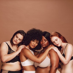 Multiracial group women in lingerie hugging each other with their eyes closed. Women of different we...