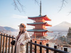 A young woman stands in front of a beautiful view of a temple and Fuji Mountain in Japan.