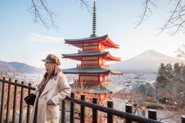 A young woman stands in front of a beautiful view of a temple and Fuji Mountain in Japan.
