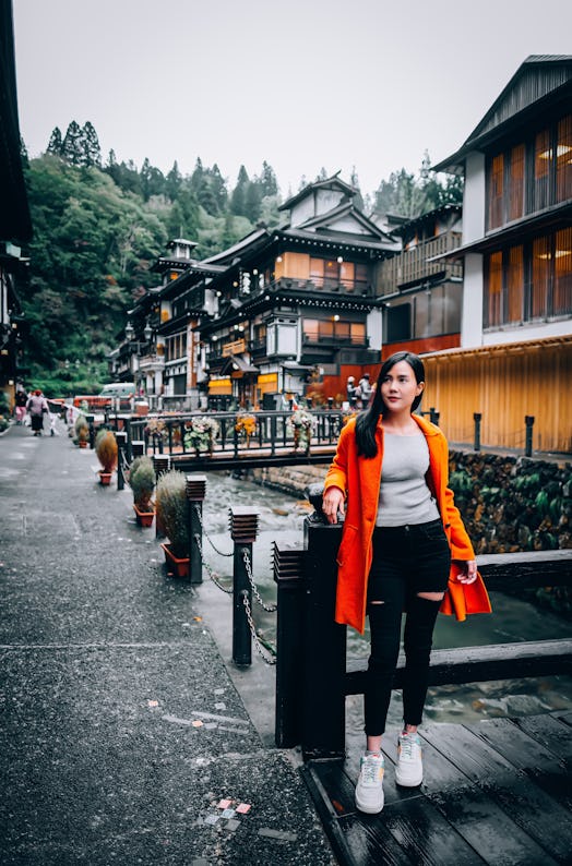 A young woman poses for a photography in a bright red jacket while traveling in Japan.