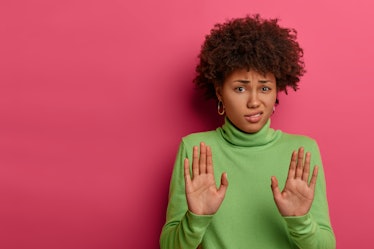 Awkward unimpressed woman with Afro hairstyle, pulls palms towards camera, refuses something, reject...