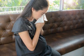 Pretty young pregnant woman feeling sick with a cold and holding a tissue in front of her nose