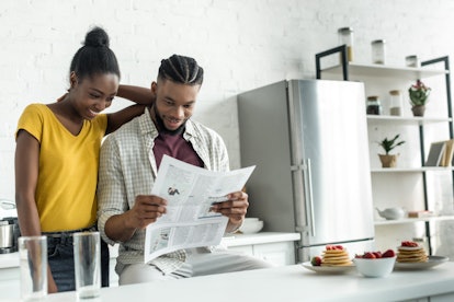 african american couple reading newspaper together at kitchen