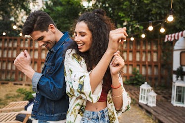 A happy couple dances back to back out in the backyard. 