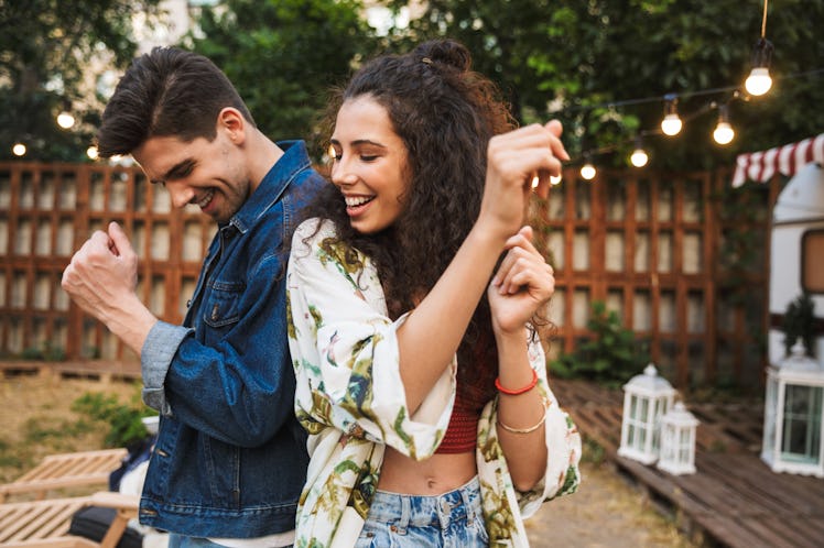A happy couple dances back to back out in the backyard.
