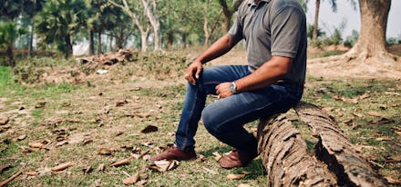 Man wearing jeans sitting on a dead parts of a tree